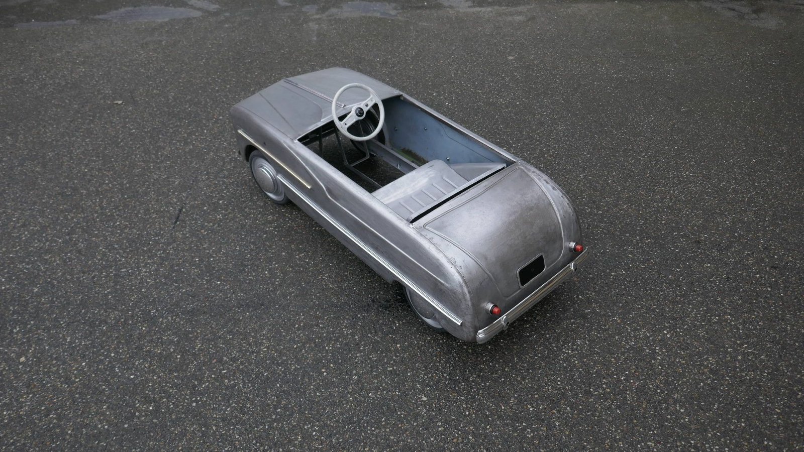 Am Straßenrand parkt ein silbernes Tretauto.